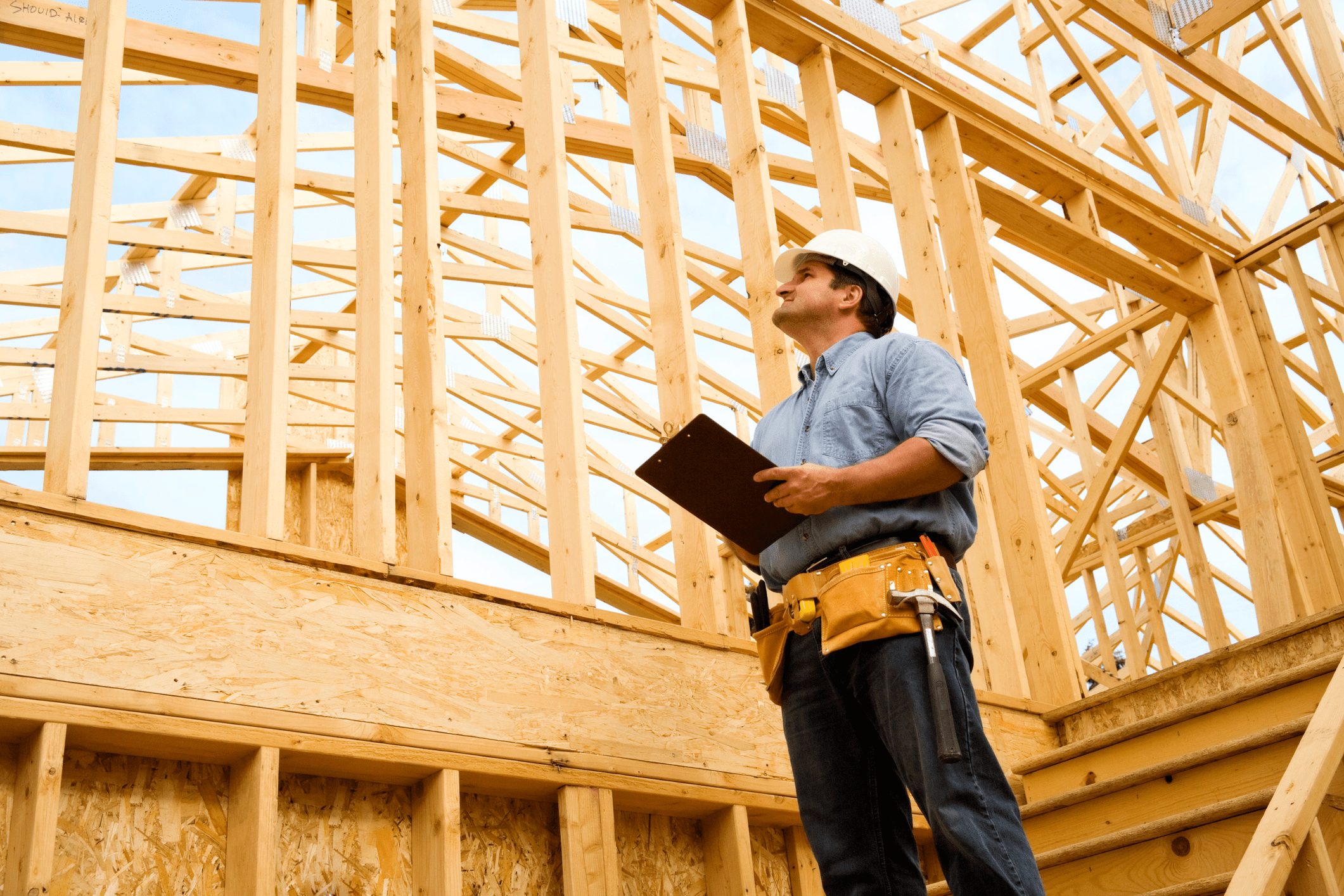 Construction worker inspecting wooden house framing with clipboard