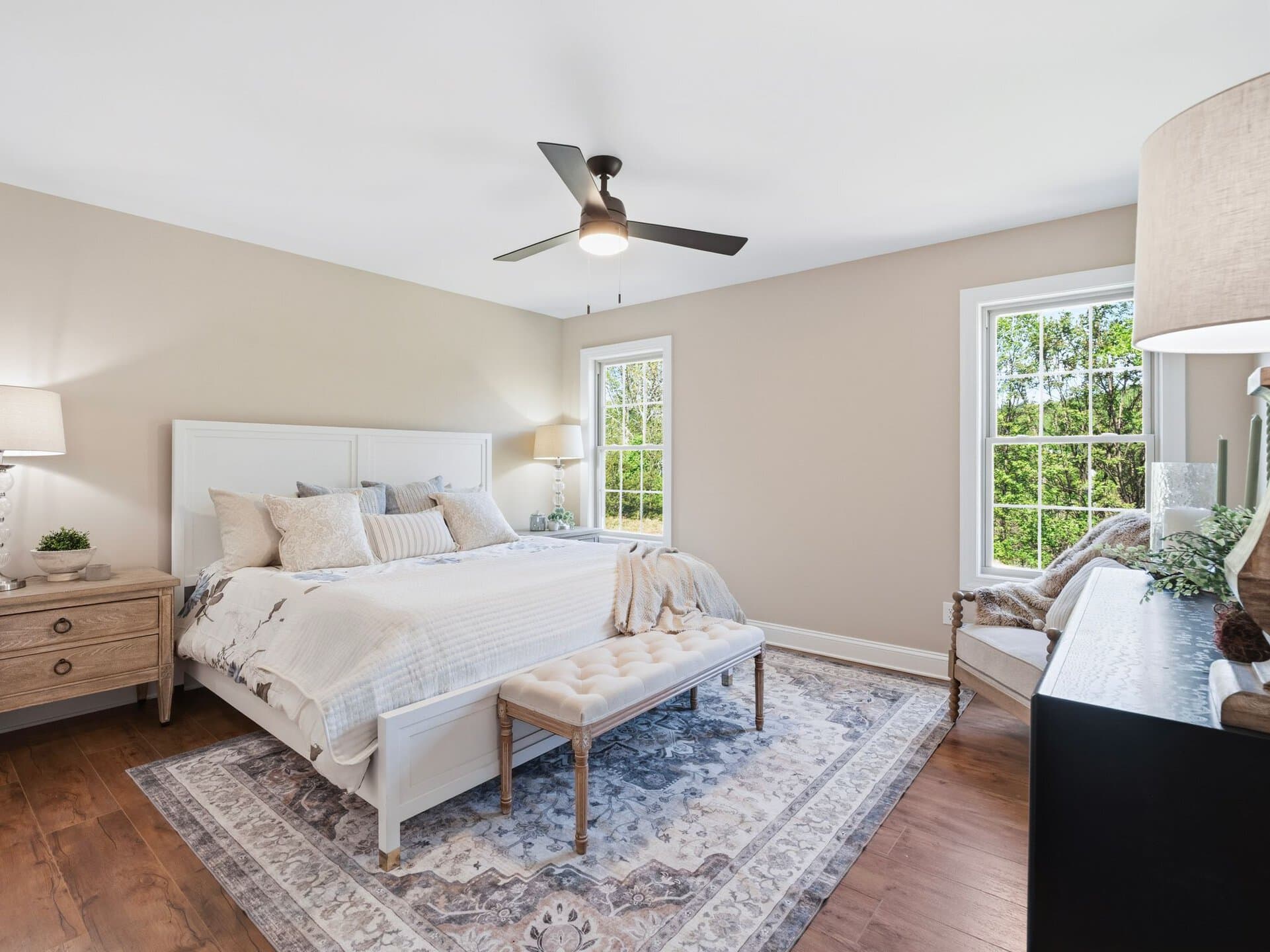 Bright bedroom with large windows, white bedding, and stylish furniture.