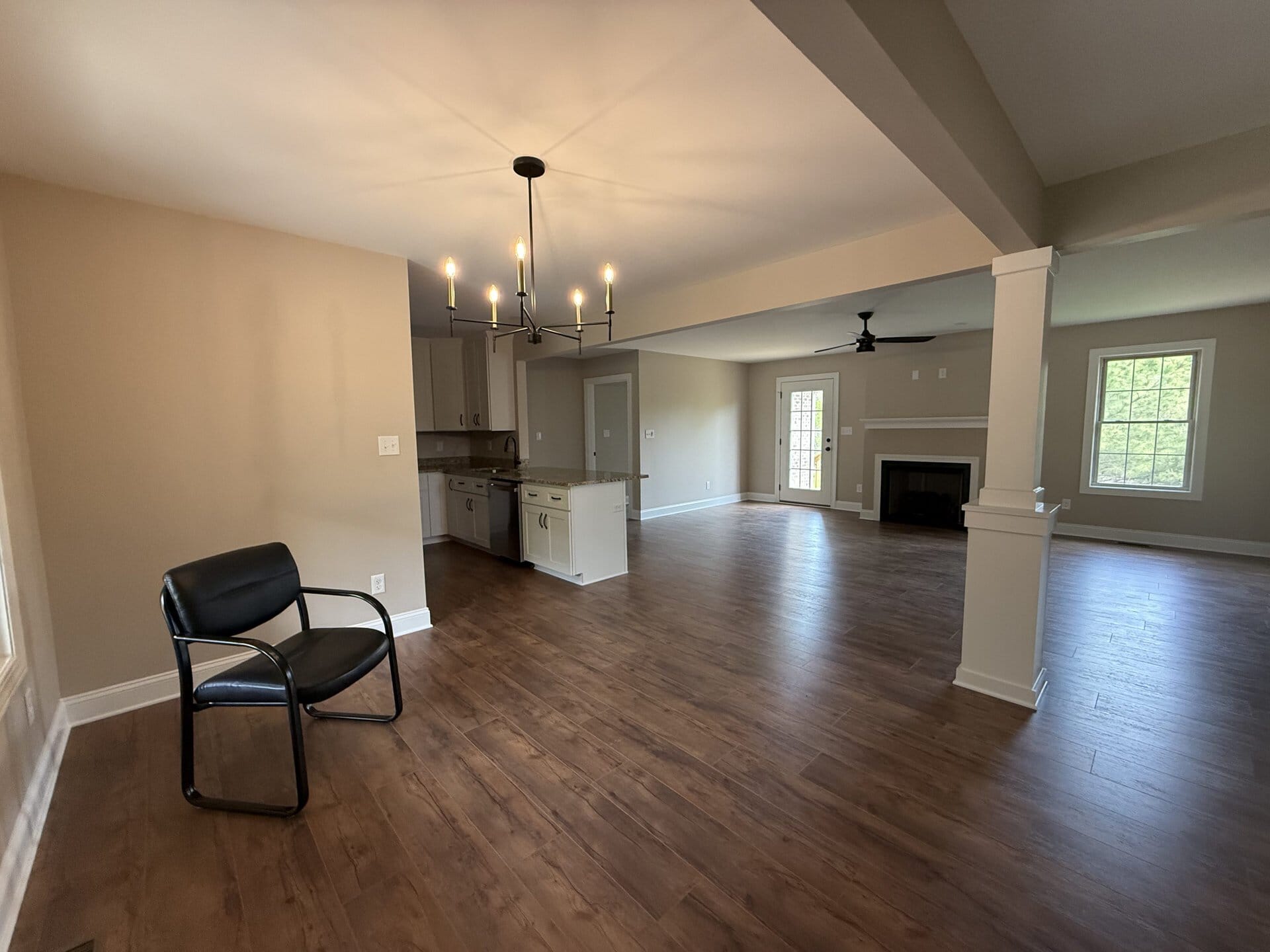 Bright open living space with hardwood floors, chandelier, and large windows.