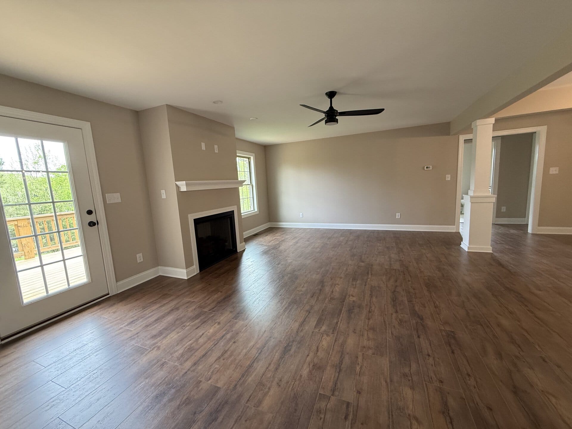 Bright living room with hardwood flooring, fireplace, ceiling fan, and large windows.